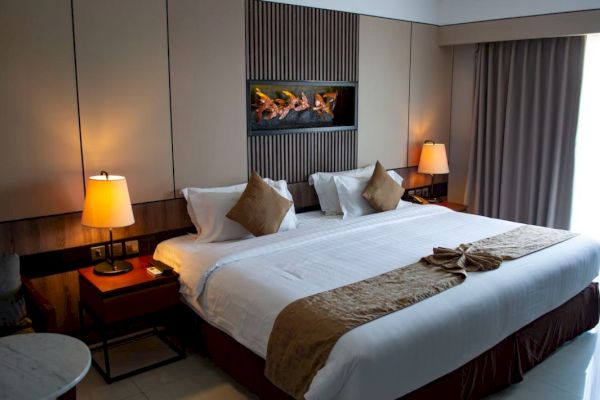 A hotel room with a large bed, two side tables with lamps, and neutral-toned decor. A modern art piece hangs above the bed.