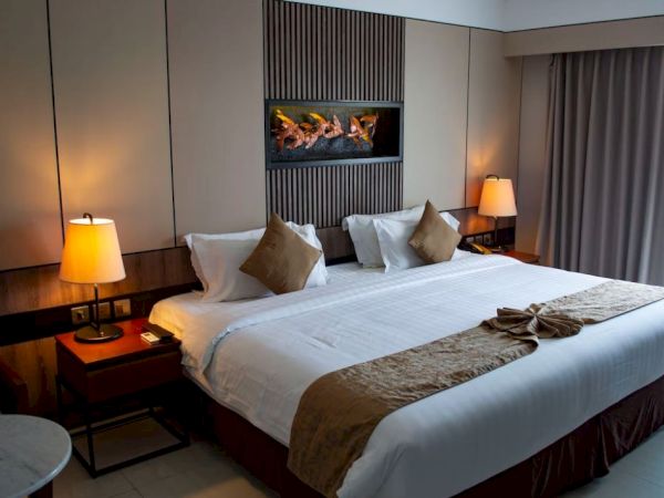 A hotel room with a large bed, two side tables with lamps, and neutral-toned decor. A modern art piece hangs above the bed.