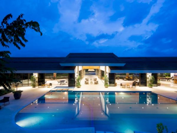 Luxurious pool area illuminated at night, with a modern open building in the background and a clear blue sky above.