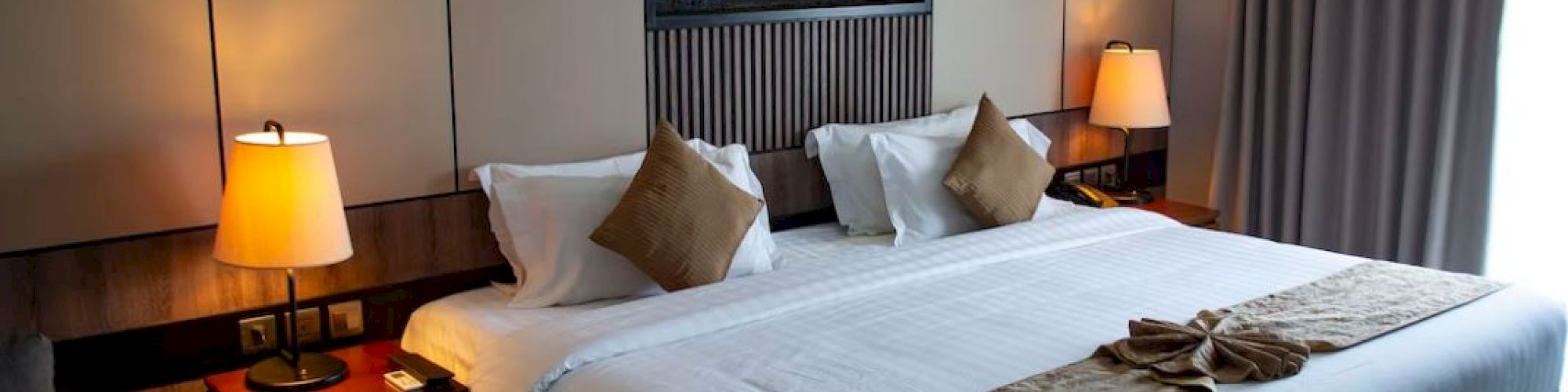 A cozy hotel room with a large bed, warm lighting, decorative pillows, and a modern wall design, creating a comfortable ambiance.