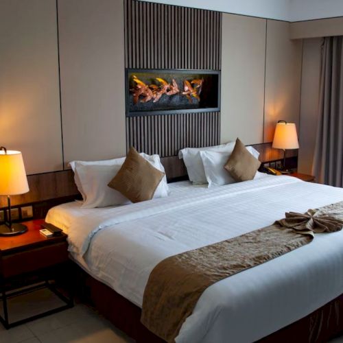 A well-lit hotel room with a large bed, two lamps, decorative pillows, and a unique wall art above the headboard.