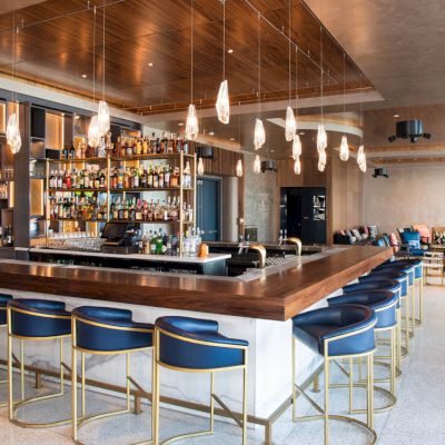 A modern bar with stylish seating, pendant lighting, and a well-stocked counter in a spacious, contemporary setting.