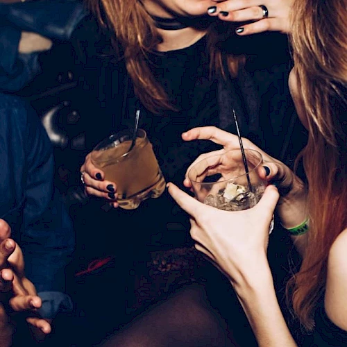 People are enjoying drinks and sharing laughter, holding beverages in a social setting.