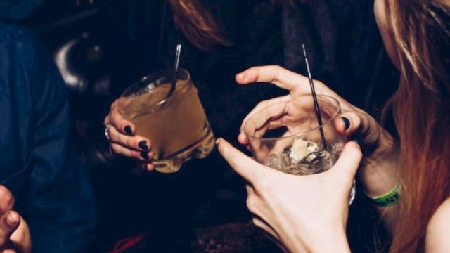 People are enjoying drinks and sharing laughter, holding beverages in a social setting.