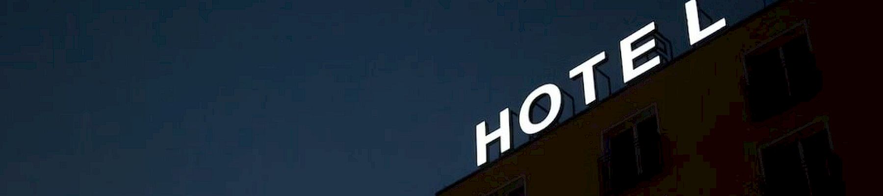 A dark silhouette of a building with an illuminated "HOTEL" sign missing the letter "E" against a night sky.