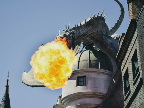 A dragon on top of a building breathing fire, set against a clear sky, with architectural details visible on the building.