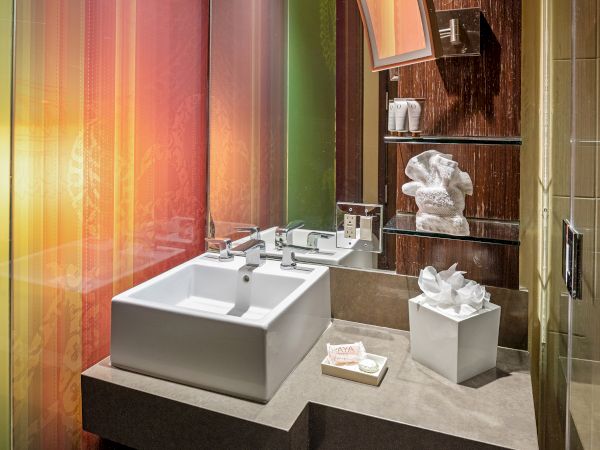 A modern bathroom with a square sink, colorful walls, toiletries, and towels arranged on shelves and a countertop.