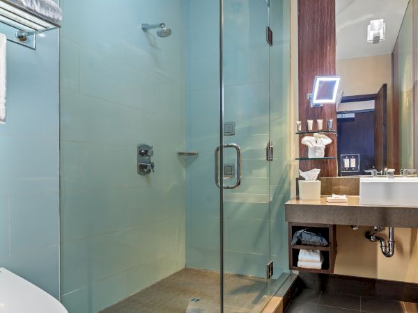 The image features a modern bathroom with a glass-enclosed shower, a sink with a mirror, and towels on a rack.