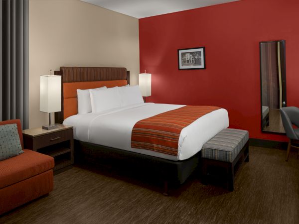 The image shows a hotel room with a large bed, bedside tables, a sofa, and a desk. The walls are red and beige.