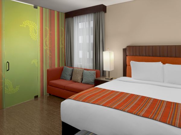 A hotel room with a bed, orange-striped bedding, a sofa, a lamp, and a decorative green sliding door.