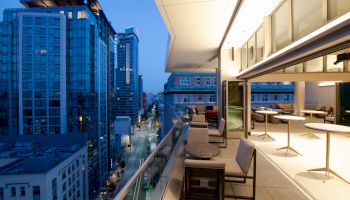 A modern city view at dusk with skyscrapers and a stylish balcony showcasing outdoor seating and tables.
