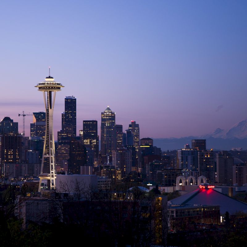 Seattle skyline at dusk with the Space Needle and Mount Rainier visible in the background, under a twilight sky.