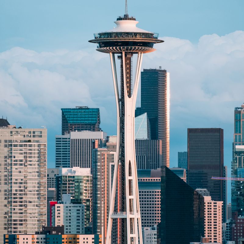 The image shows the Space Needle in Seattle, surrounded by skyscrapers and a partly cloudy sky backdrop.