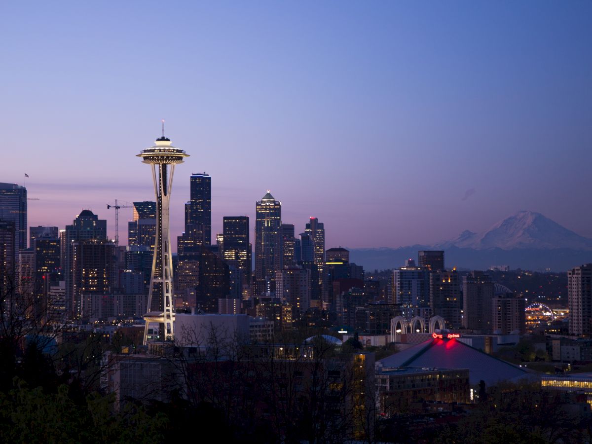 Seattle skyline at dusk, featuring the Space Needle with city buildings and Mount Rainier in the background under a twilight sky.
