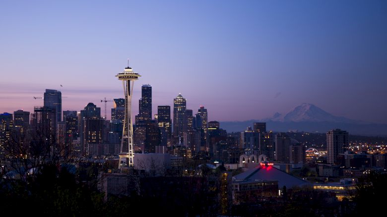 Seattle skyline at dusk, featuring the Space Needle with city buildings and Mount Rainier in the background under a twilight sky.