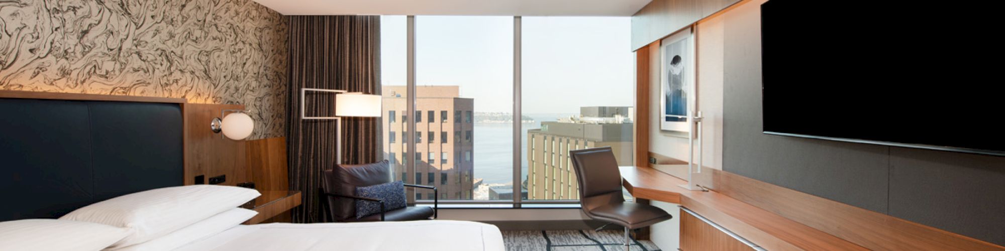 A modern hotel room with a large bed, a desk, a chair, a wall-mounted TV, and a city view through the window ends the sentence.
